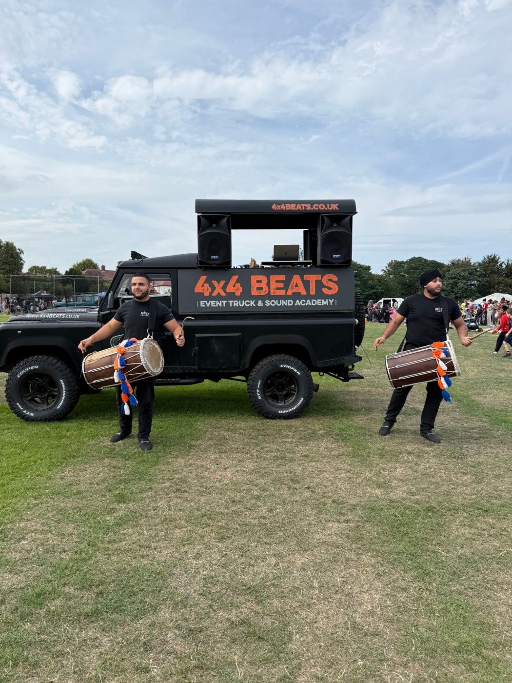 Two dhol players performing beside the 4x4 Beats sound truck at an outdoor community event